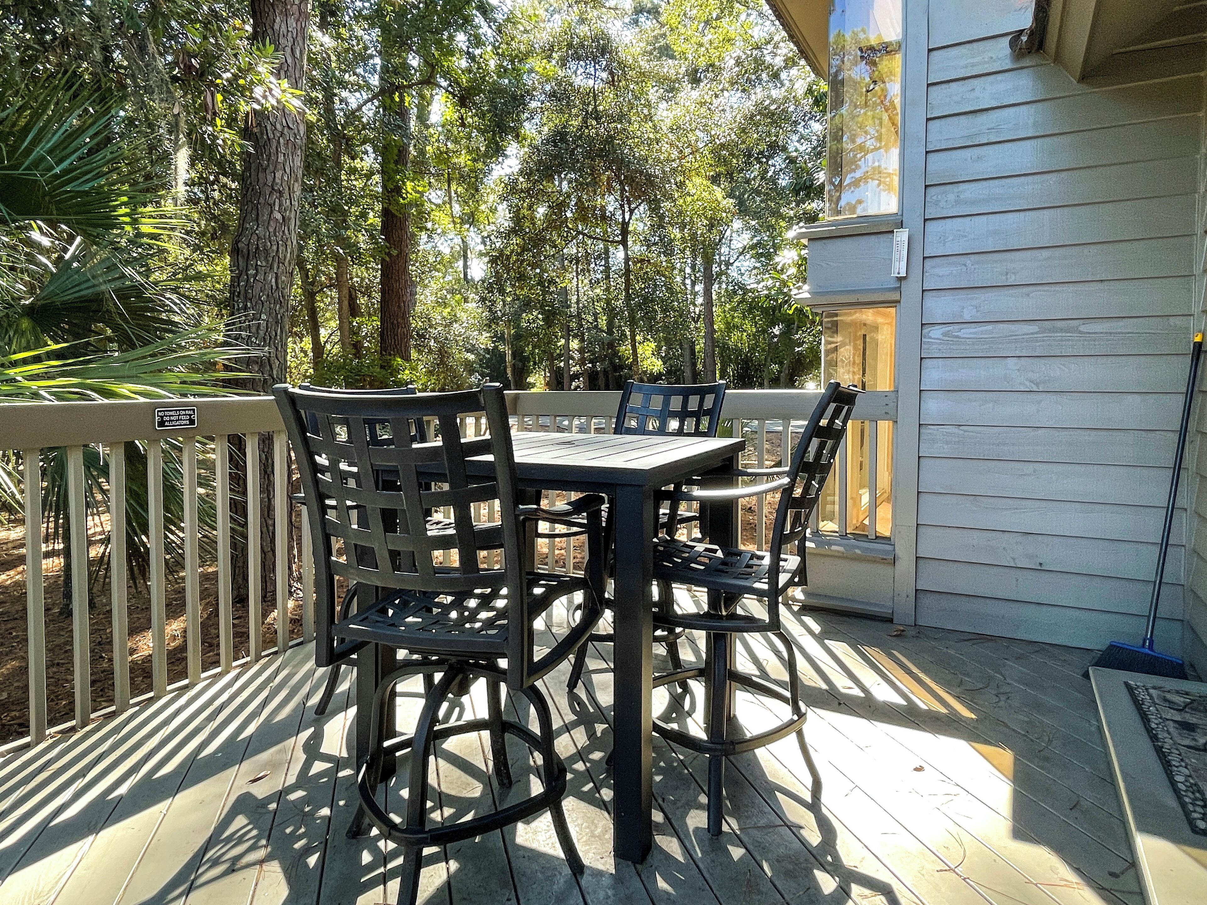 A wooden deck with a table and chairs, surrounded by a white fence and trees.