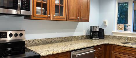 Una cocina con armarios de madera, microondas de acero inoxidable, estufa y cafetera.