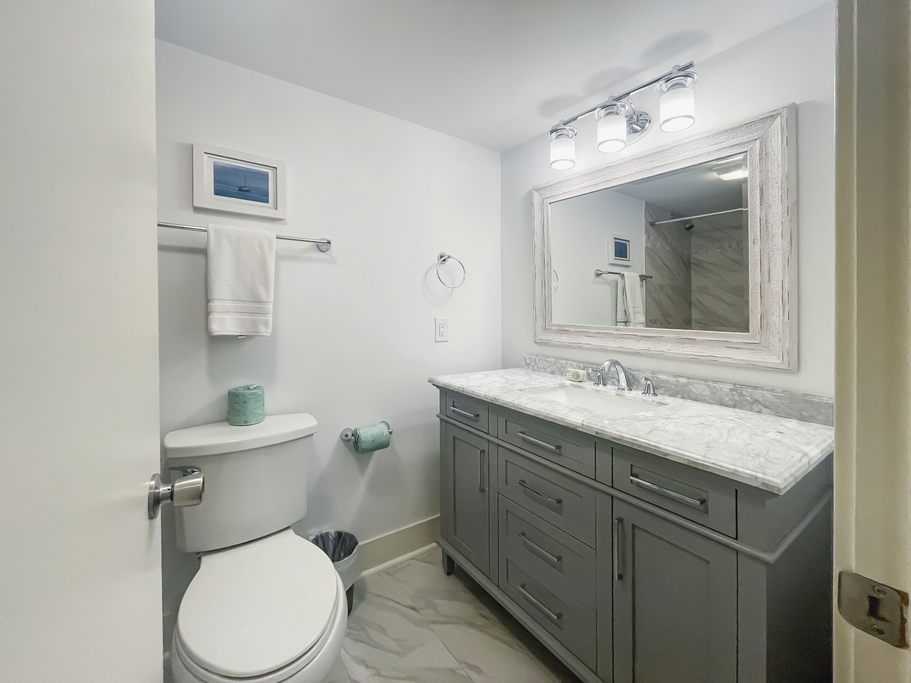 A bathroom with a toilet, sink, vanity, and a large mirror.