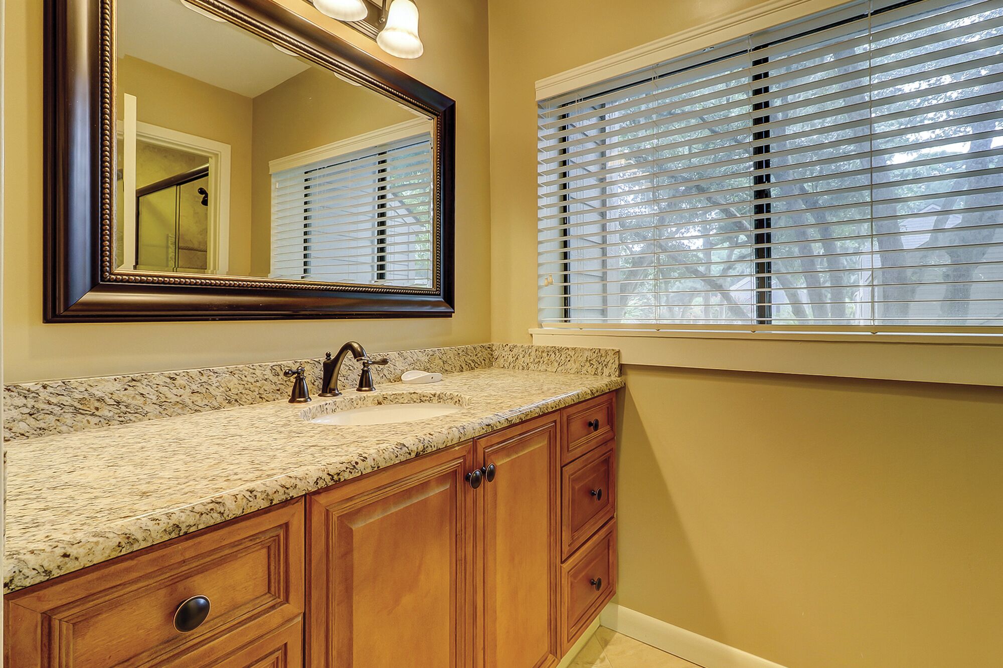 A bathroom with a granite countertop sink, wooden cabinets, and a large mirror.
