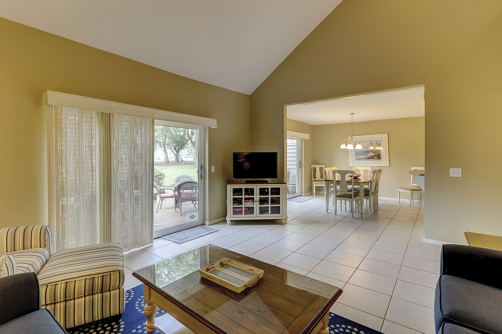 A living room with a TV, a glass coffee table, and a dining area with chairs.
