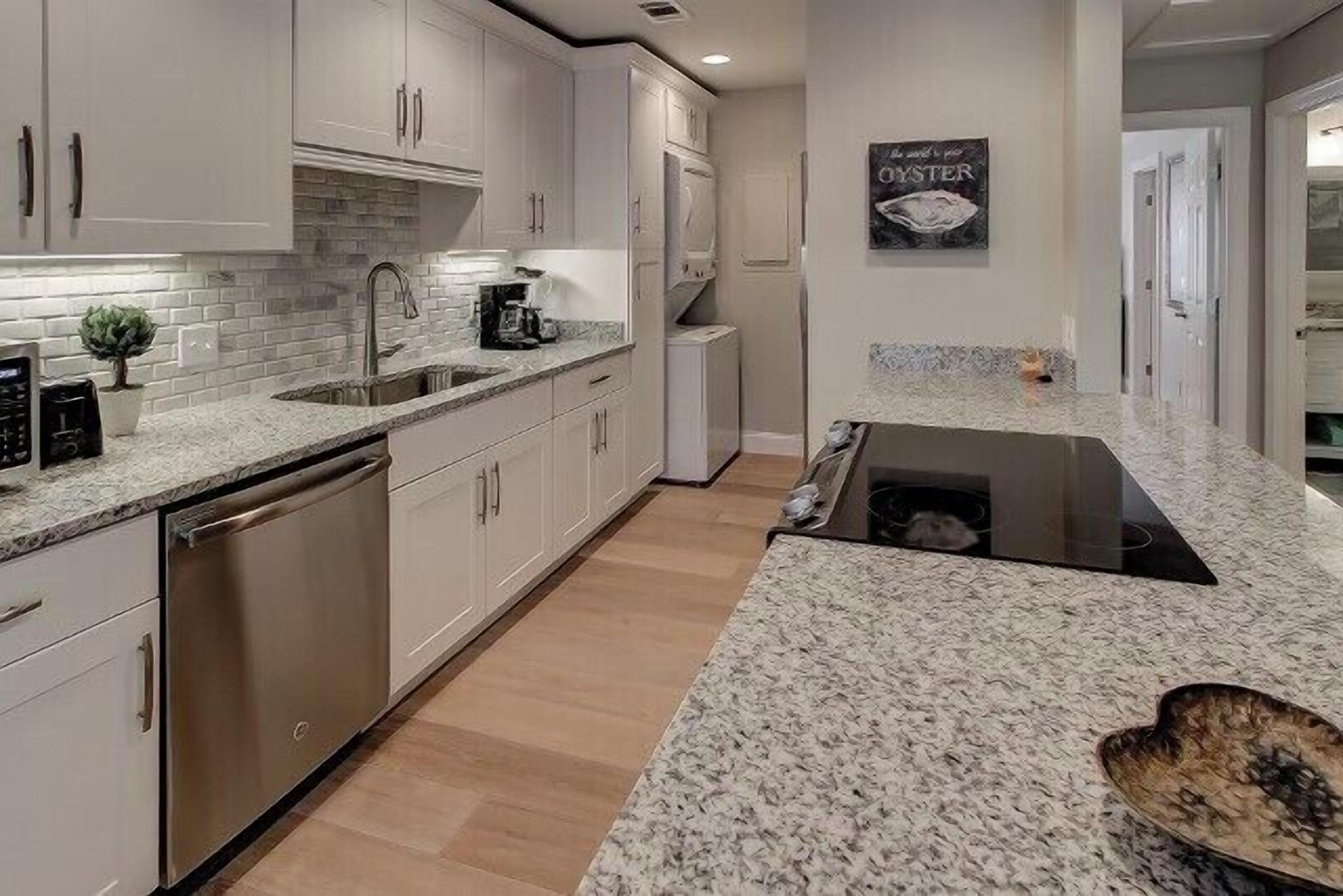 A modern kitchen with white cabinetry, a granite countertop, and a built-in dishwasher.