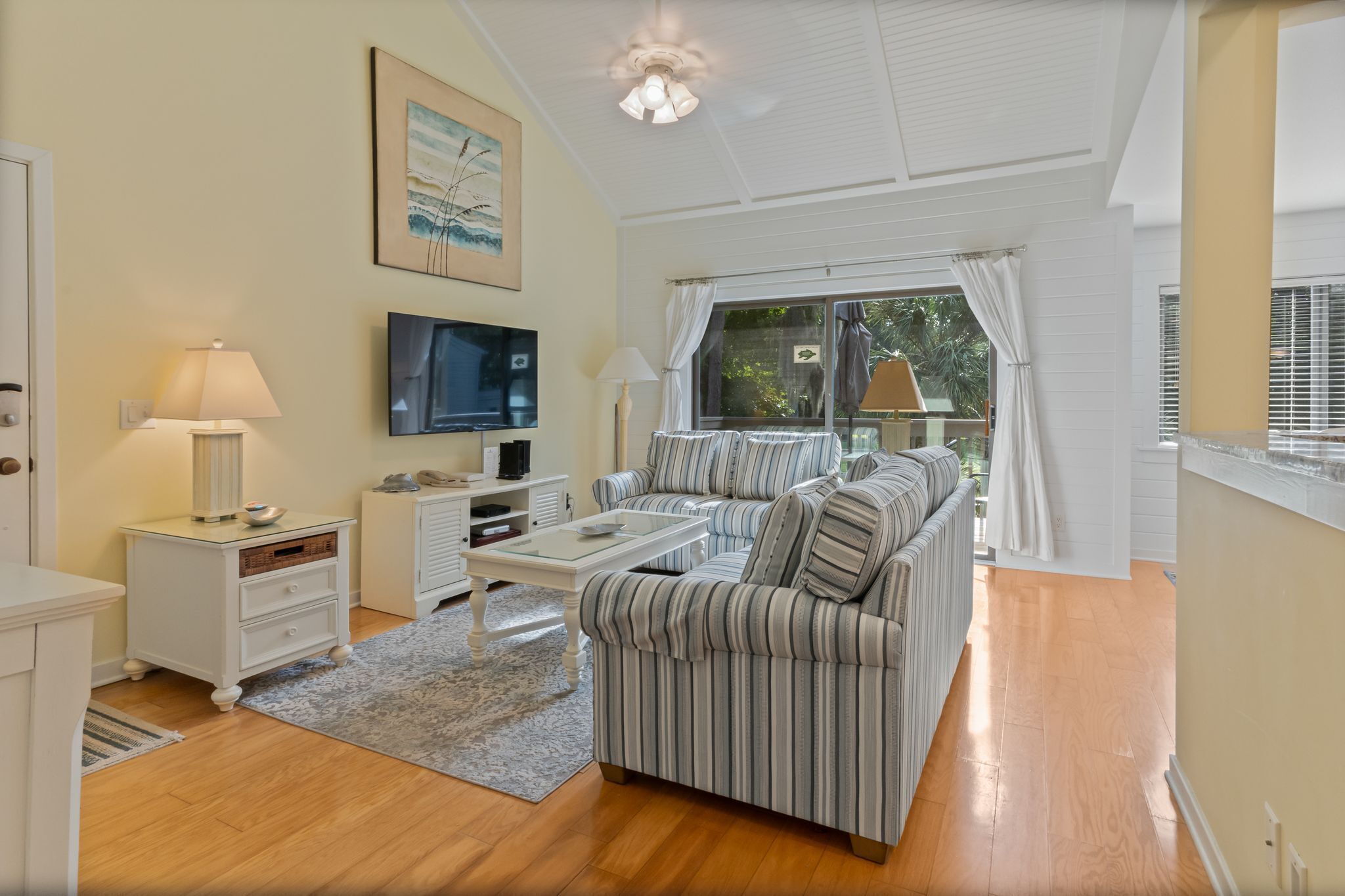 A modern living room with a striped sofa, a flat-screen TV, a coffee table, and a ceiling fan.