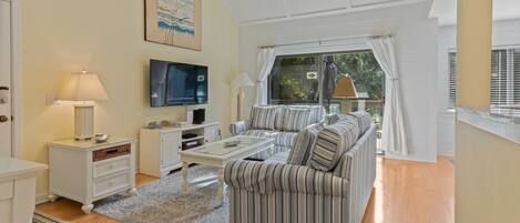 A modern living room with a striped sofa, a flat-screen TV, a coffee table, and a ceiling fan.