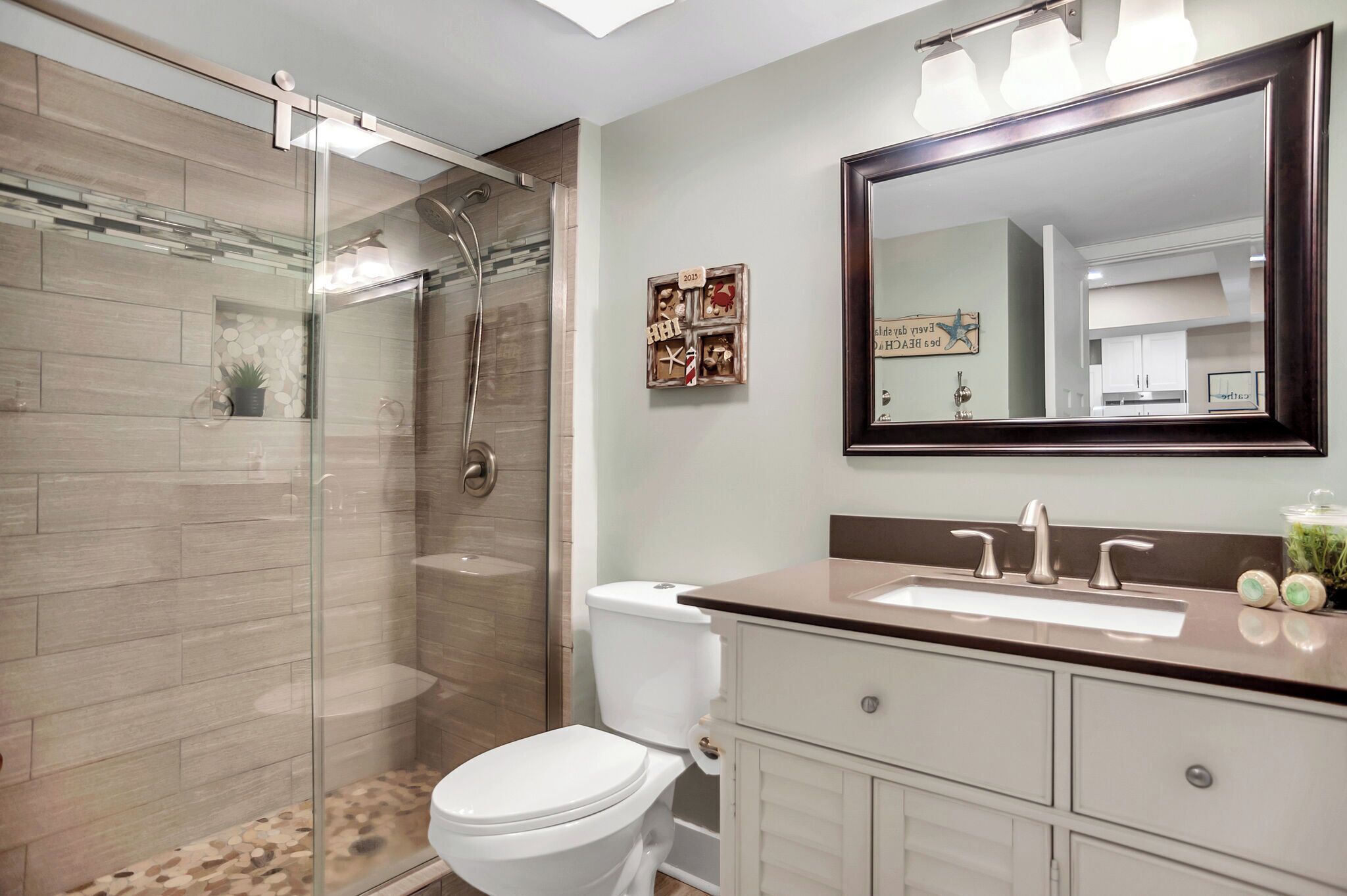 A modern bathroom with a glass-enclosed shower, a white toilet, a large mirror, and a vanity with a sink.