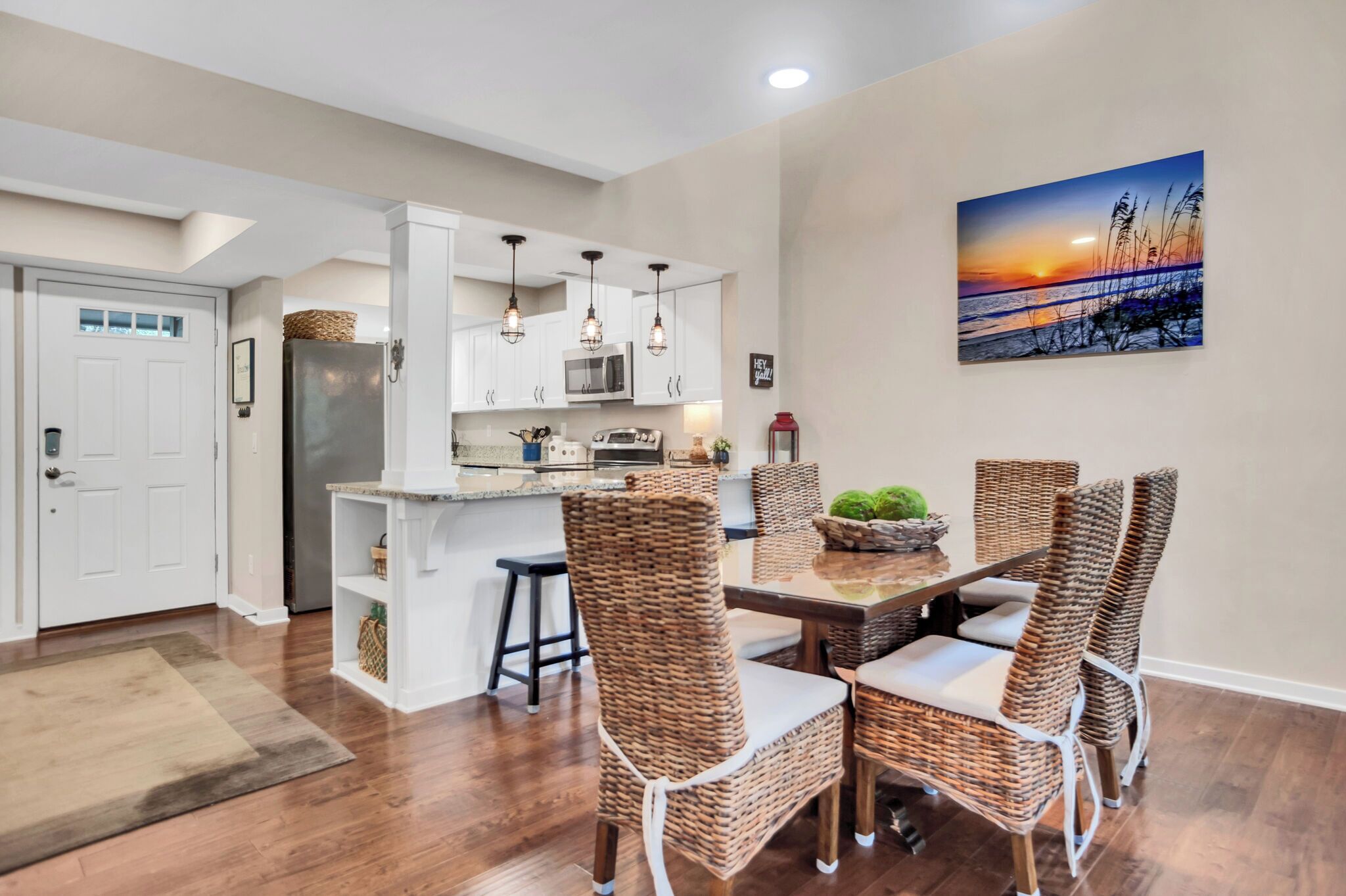 A modern kitchen with white cabinets, a stainless steel refrigerator, and hanging pendant lights.