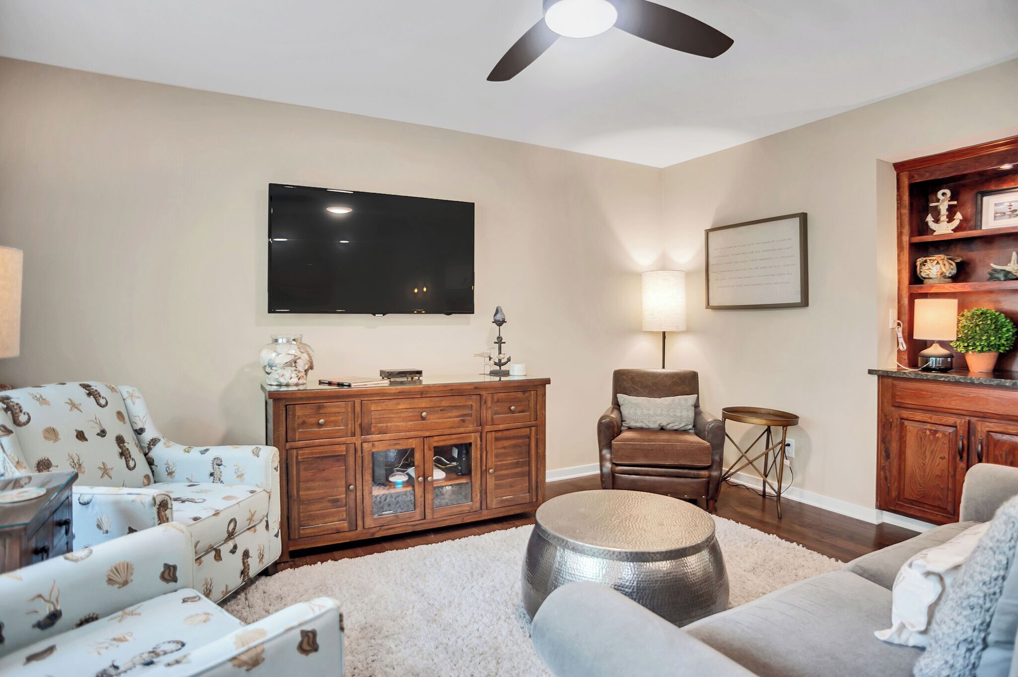A living room with a flat-screen TV, wooden furniture, a ceiling fan, and a decorative wall piece.