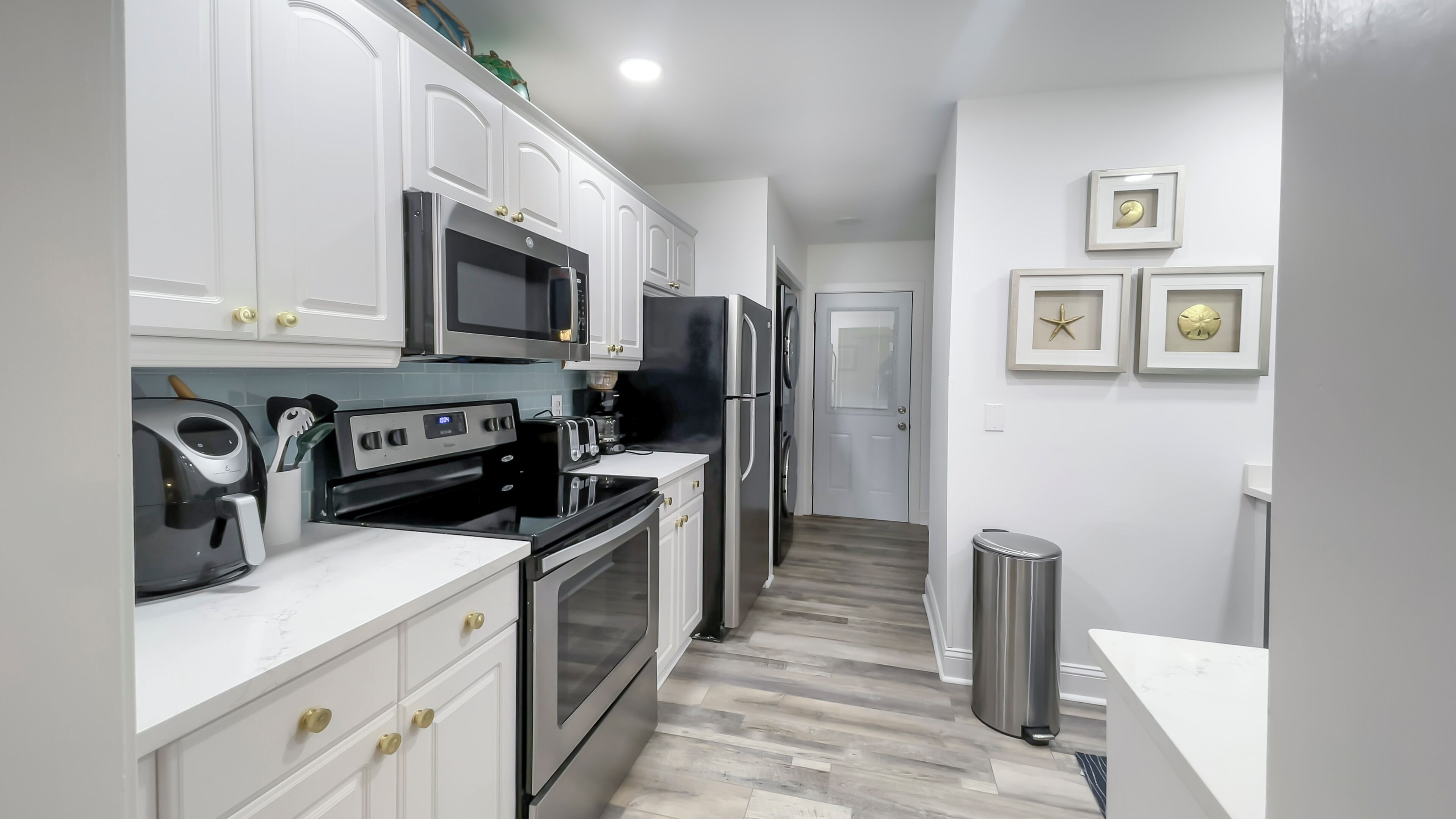 A modern kitchen with white cabinetry, stainless steel appliances, and a wood-patterned floor.