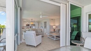 A modern living room with a sofa, armchairs, and a coffee table. There is a balcony with a glass door leading outside. - Gulf-View Escape | Bright & Breezy 2BR Condo Steps from the Beach (Sanibel)