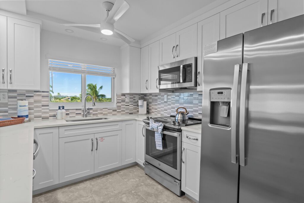 A modern kitchen with stainless steel appliances, white cabinetry, and a view of palm trees.