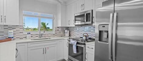 A modern kitchen with stainless steel appliances, white cabinetry, and a view of palm trees.