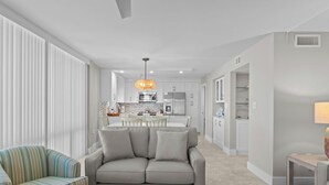 A modern living room with a sofa, a striped armchair, and a dining area with a table and chairs. - Gulf-View Escape | Bright & Breezy 2BR Condo Steps from the Beach (Sanibel)