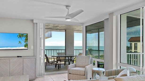 A spacious balcony with a view of the ocean, a ceiling fan, and a dining area with chairs and a table. - Gulf-View Escape | Bright & Breezy 2BR Condo Steps from the Beach (Sanibel)