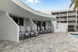 Un espace aménagé au bord de la piscine, avec un bâtiment aux lignes courbes, une piscine et un panneau indiquant qu’il est interdit de plonger.