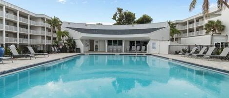 Una piscina con sillones de descanso y un edificio con balcones al fondo.
