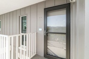 Een balkon met een witte reling, een schuifdeur en uitzicht op een parkeerplaats.