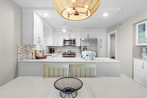 Een moderne keuken met witte kasten, een centraal eiland en een zwarte metalen stoel.