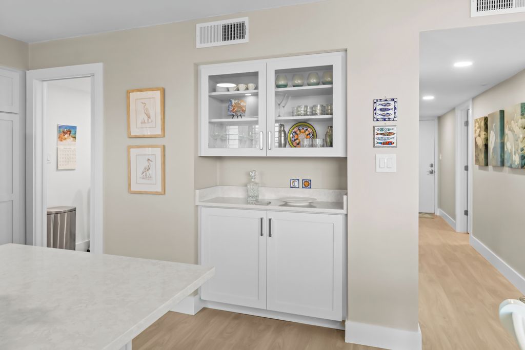 A modern kitchen with white cabinetry, a marble countertop, and a built-in oven. There are framed pictures on the wall and a small island with a sink.