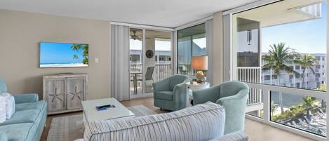A modern living room with a large balcony, a television, and a view of the ocean.