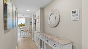 Un pasillo con suelo de madera, una consola blanca con cajones, un espejo redondo y un letrero en la pared.