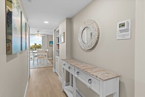 Un pasillo con suelo de madera, una consola blanca con cajones, un espejo redondo y un letrero en la pared.