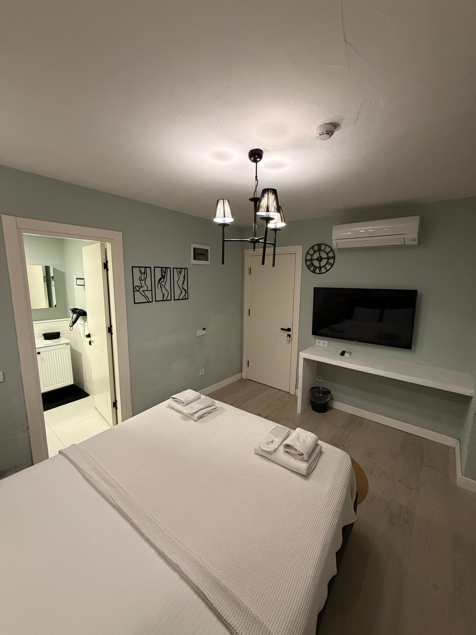 A bedroom with a bed, a TV, an air conditioner, and artwork on the wall.