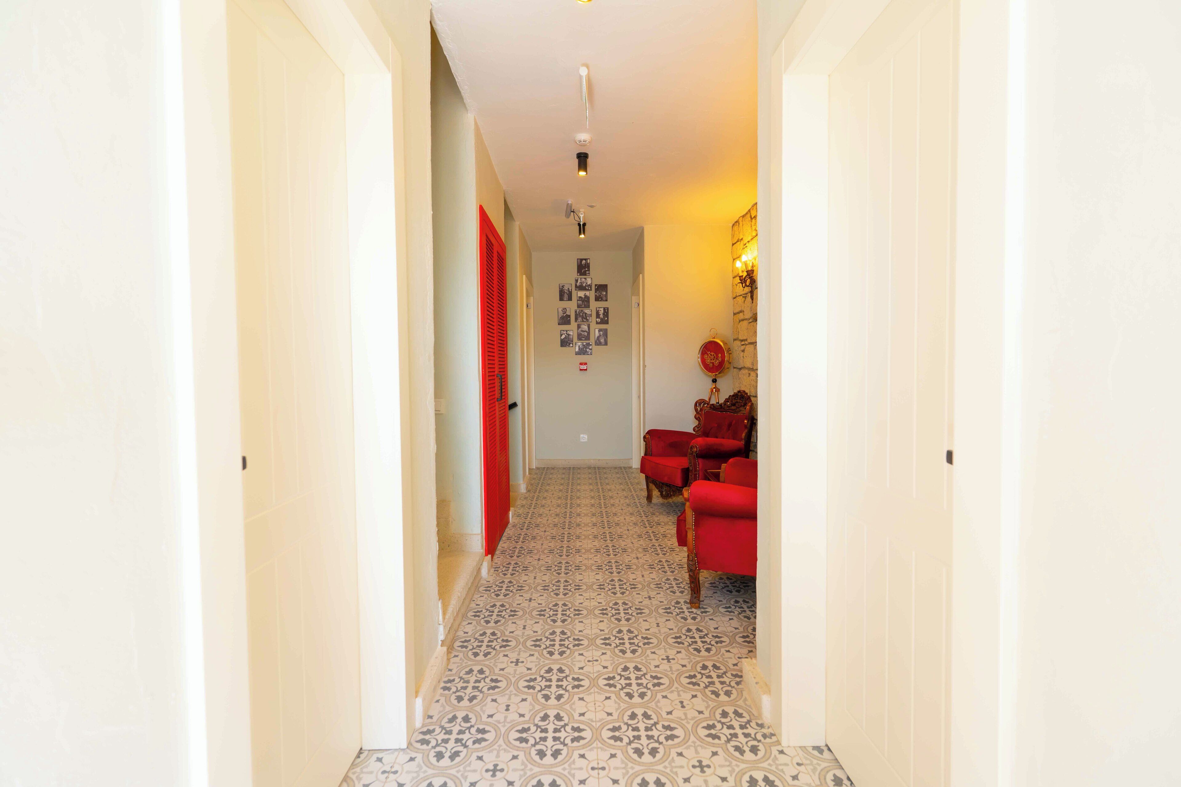 A narrow hallway with patterned floor tiles, a red door, and a red armchair.