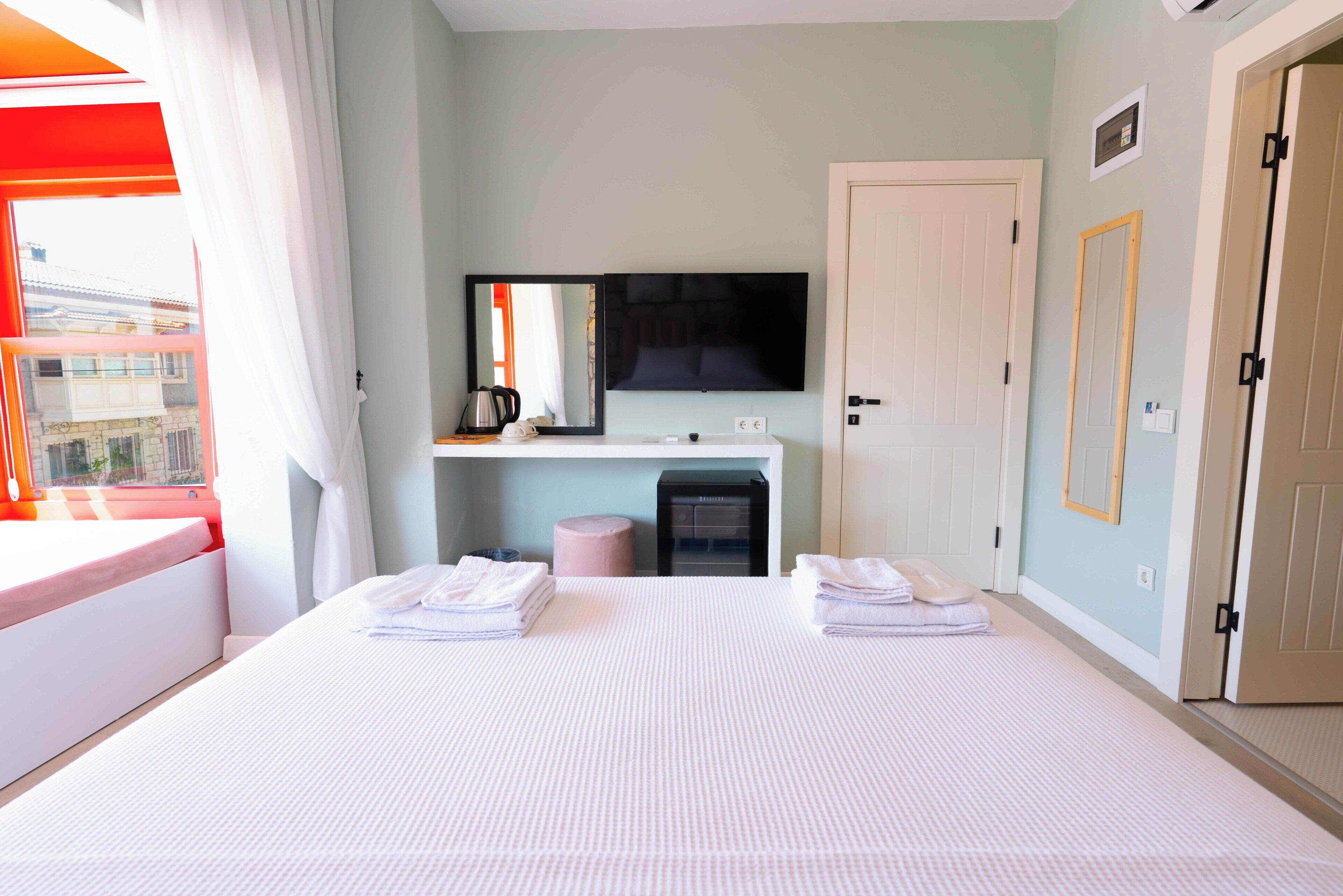 Une chambre d’hôtel avec un grand lit, un téléviseur fixé au mur, un bureau avec un miroir et une porte.