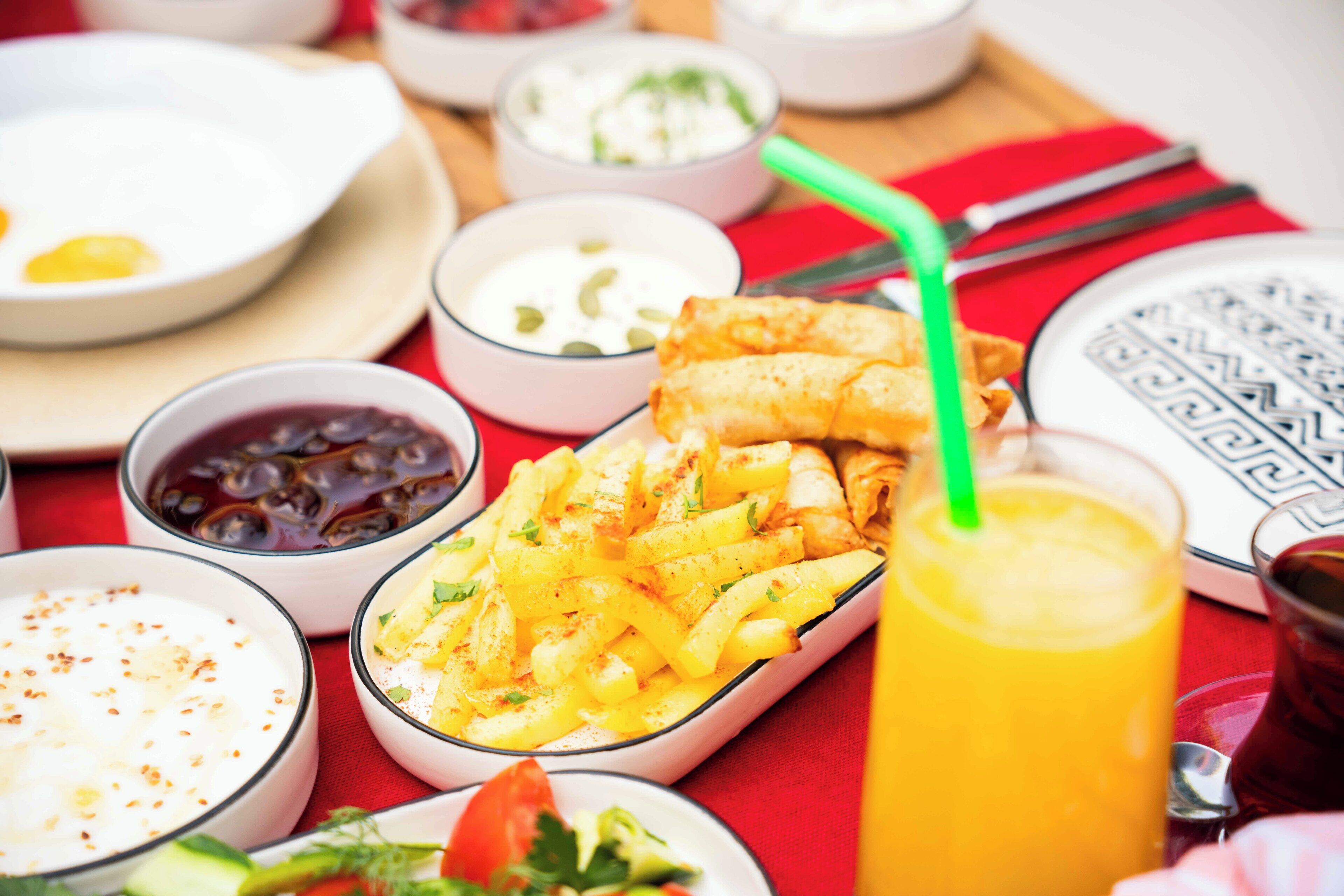 A table with various dishes including fried items, bowls of soup, and a glass of orange juice.