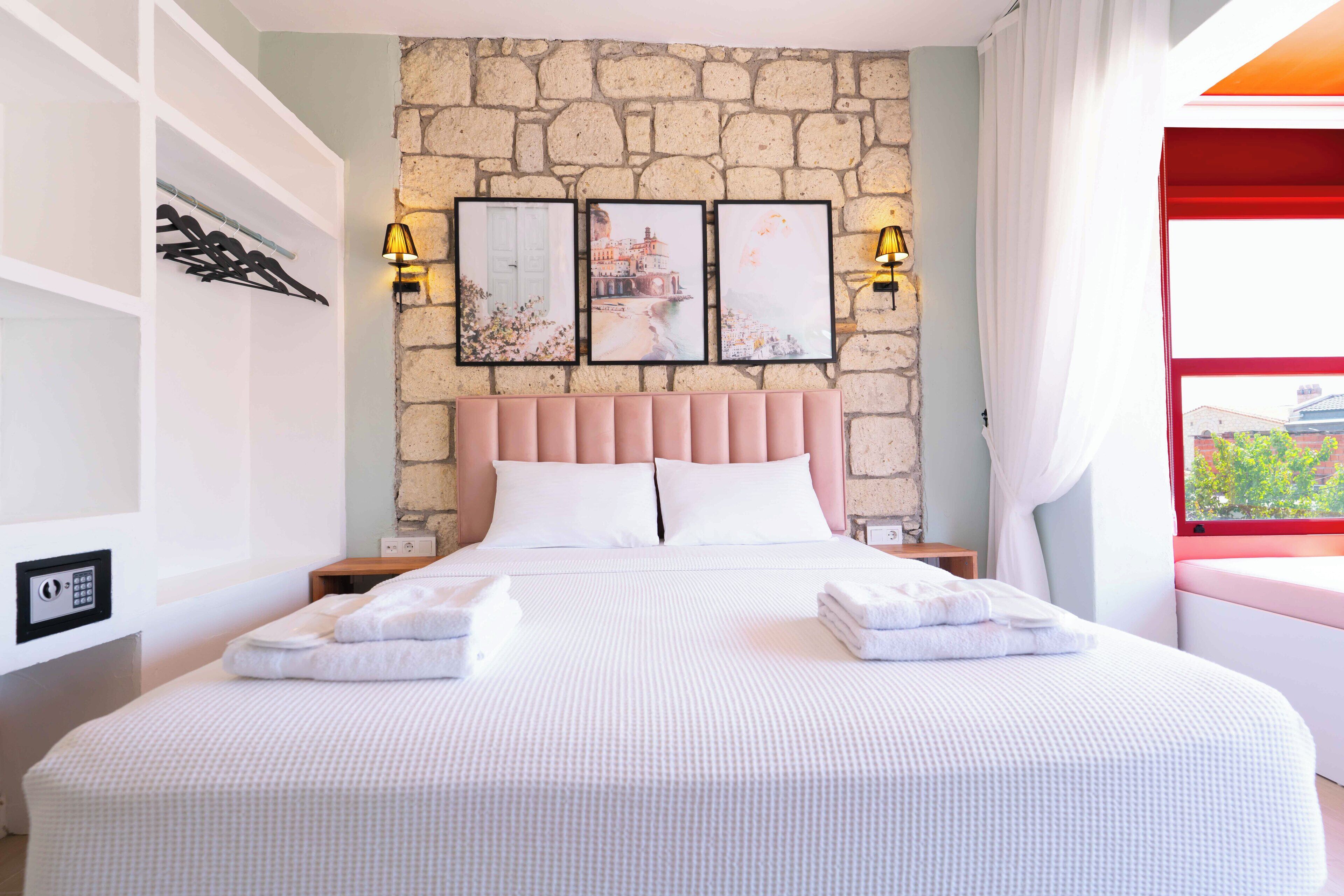 A neatly made bed with white linens and two pillows, a stone wall behind, and three framed pictures above.