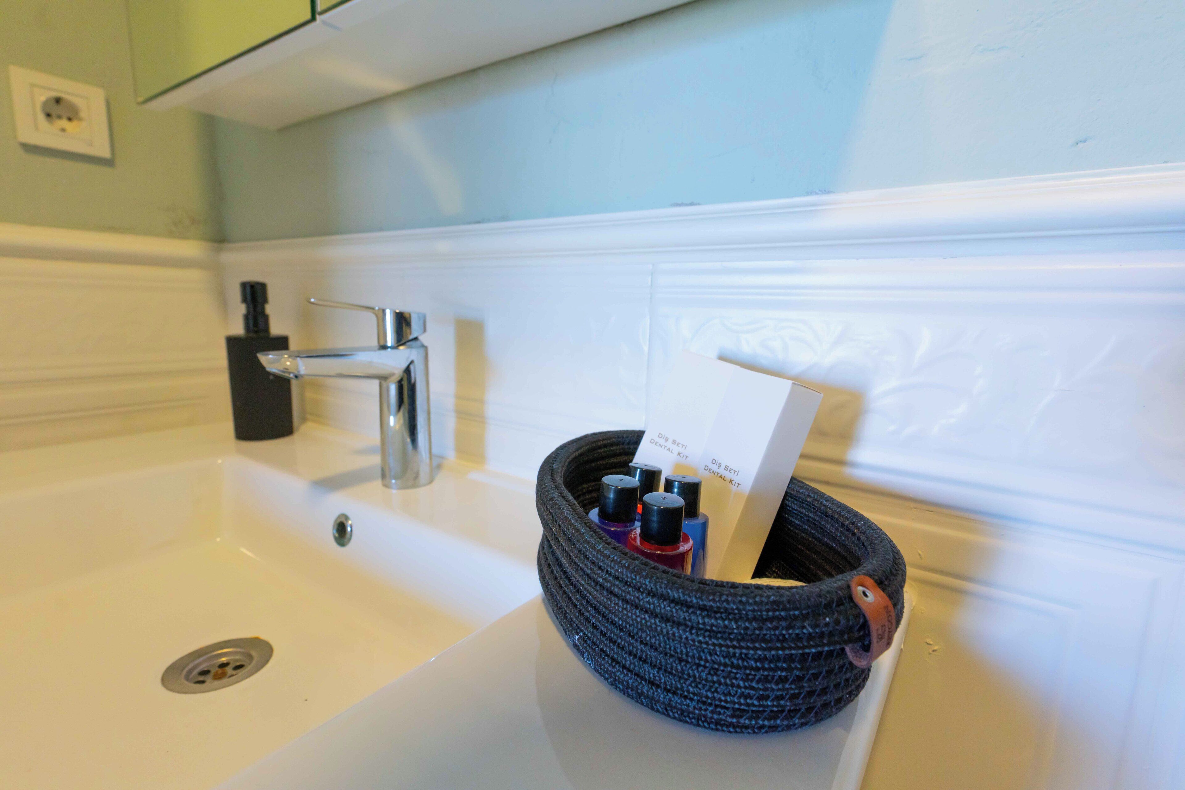 Un lavabo de salle de bain avec un porte-serviettes noir tressé contenant des articles de toilette.
