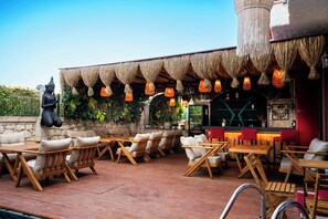 An outdoor seating area with wooden tables and chairs, a statue, and hanging lanterns. - Karnelyan Alaçatı (Cesme)