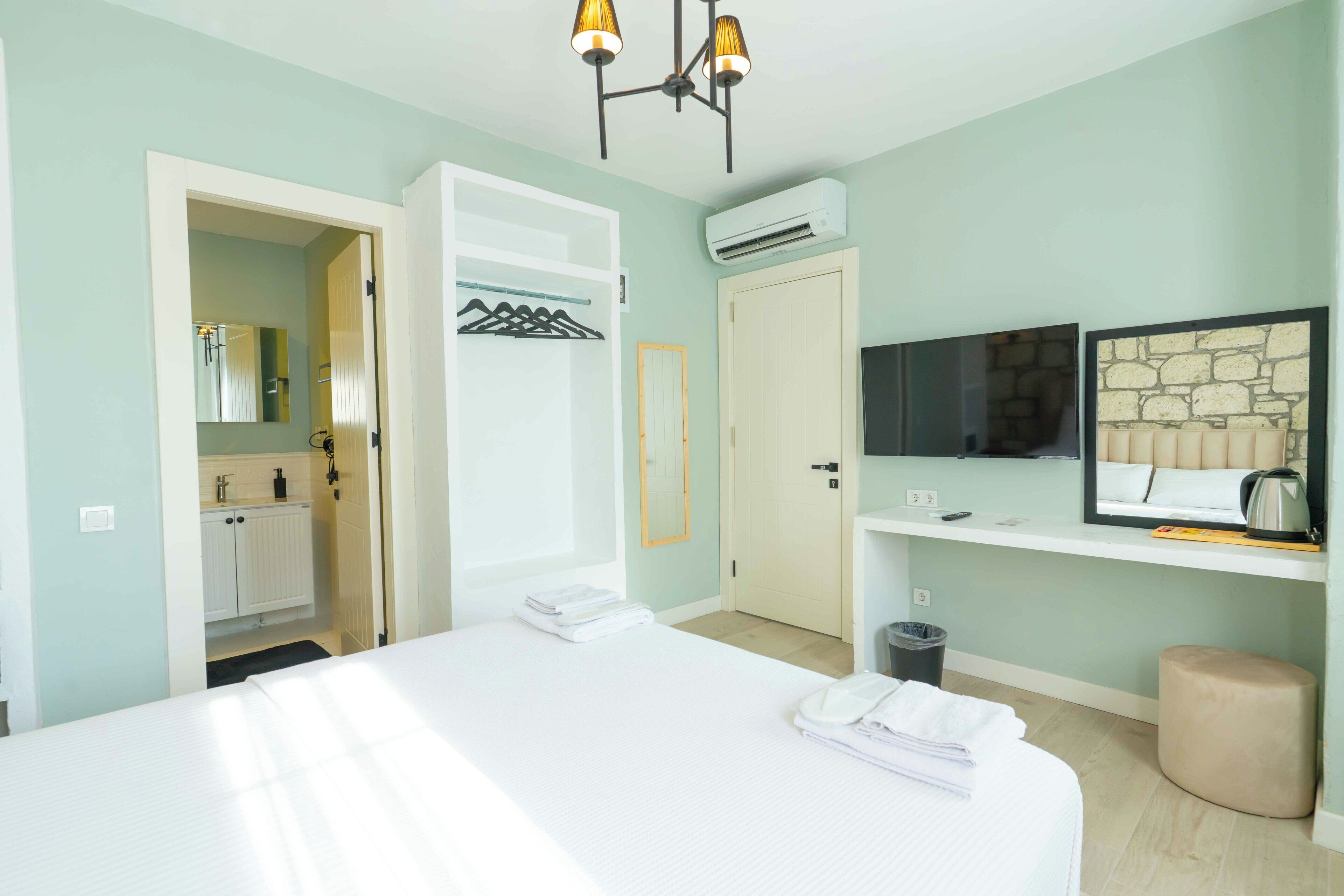 A hotel room with a bed, a wardrobe, a mirror, an air conditioning unit, a television, and a small seating area.