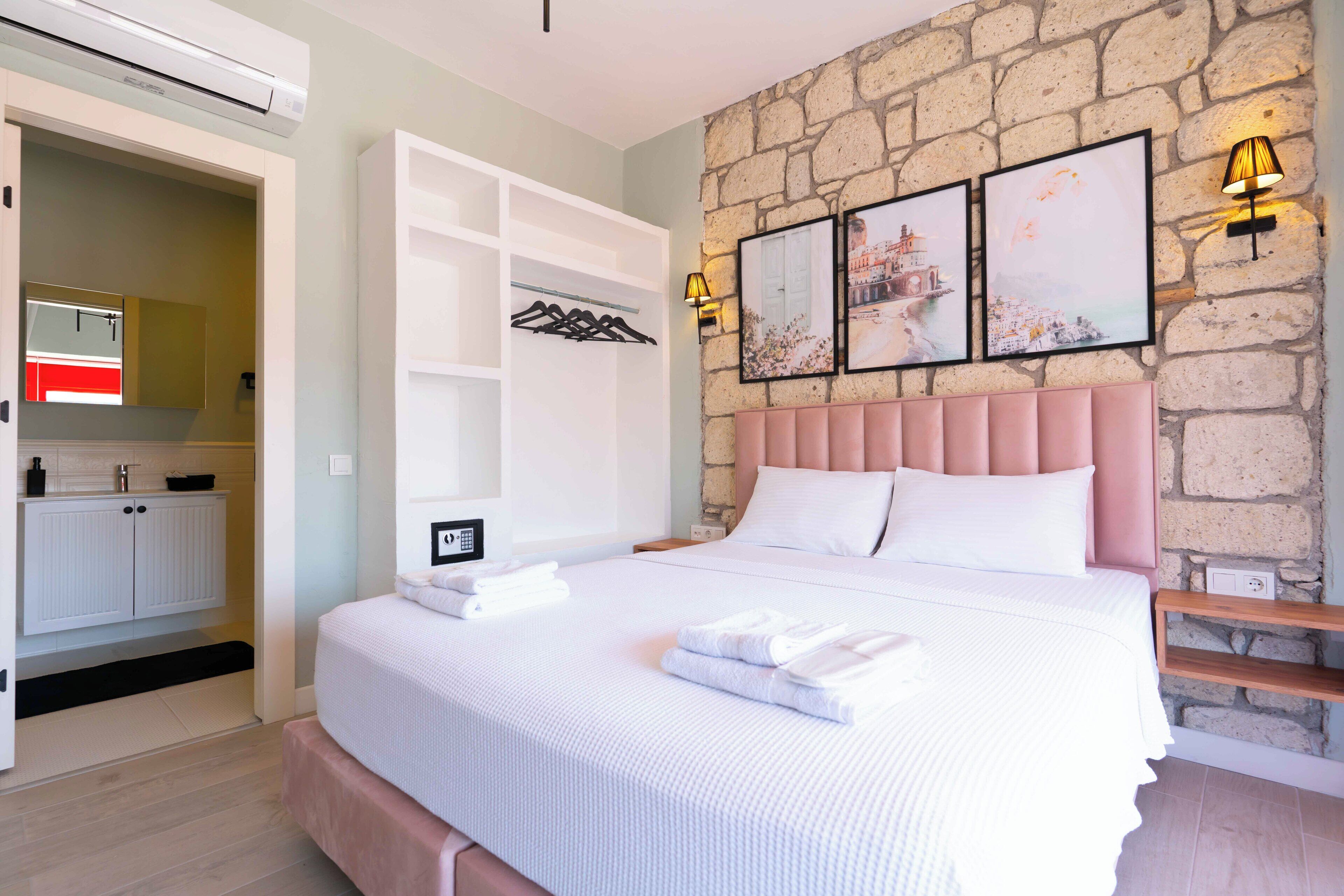 A bedroom with a stone wall, a bed with white bedding, a pink headboard, and a wall-mounted light fixture.