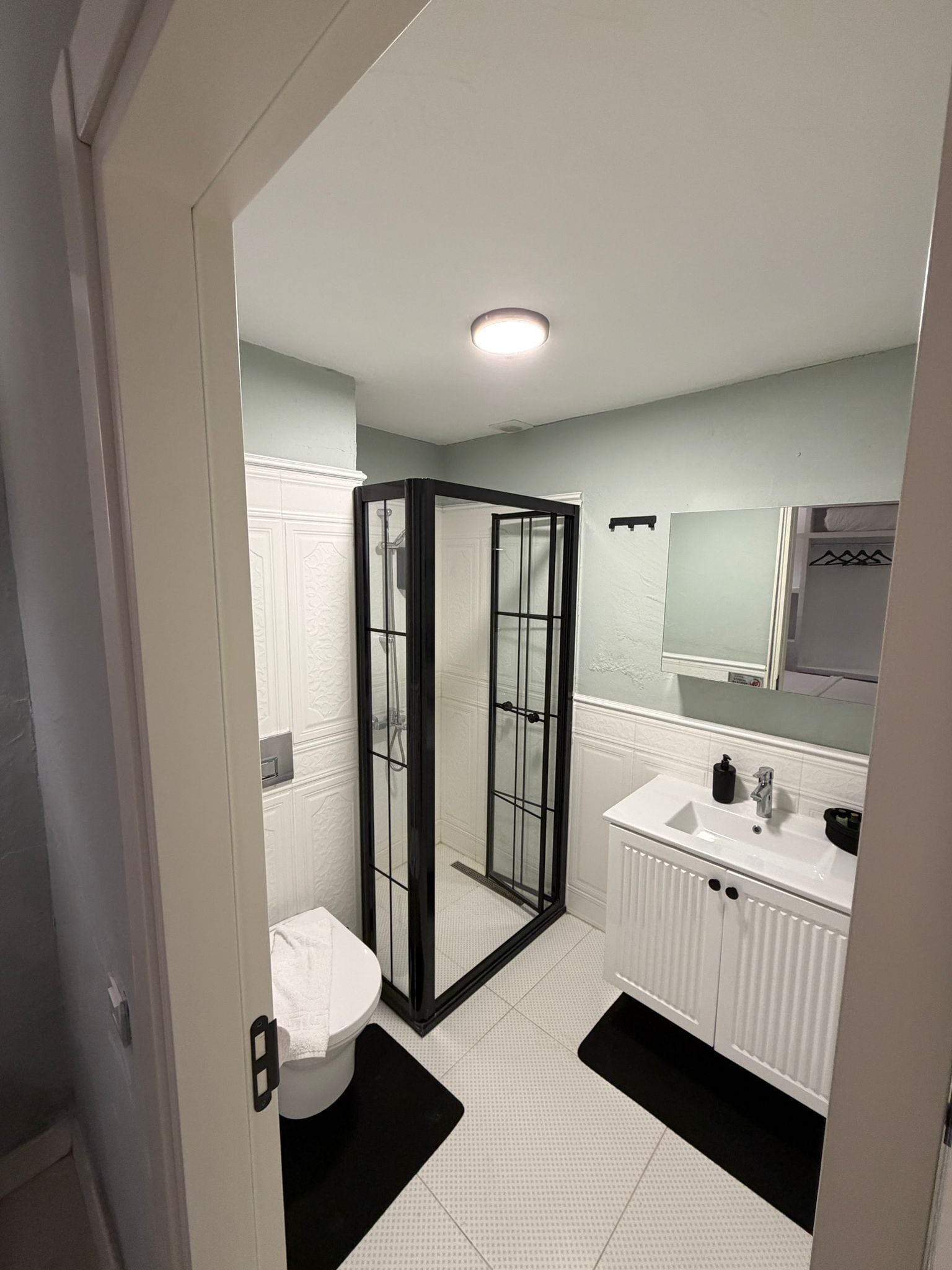 A modern bathroom with a glass shower enclosure, white cabinetry, and a large mirror above the sink.