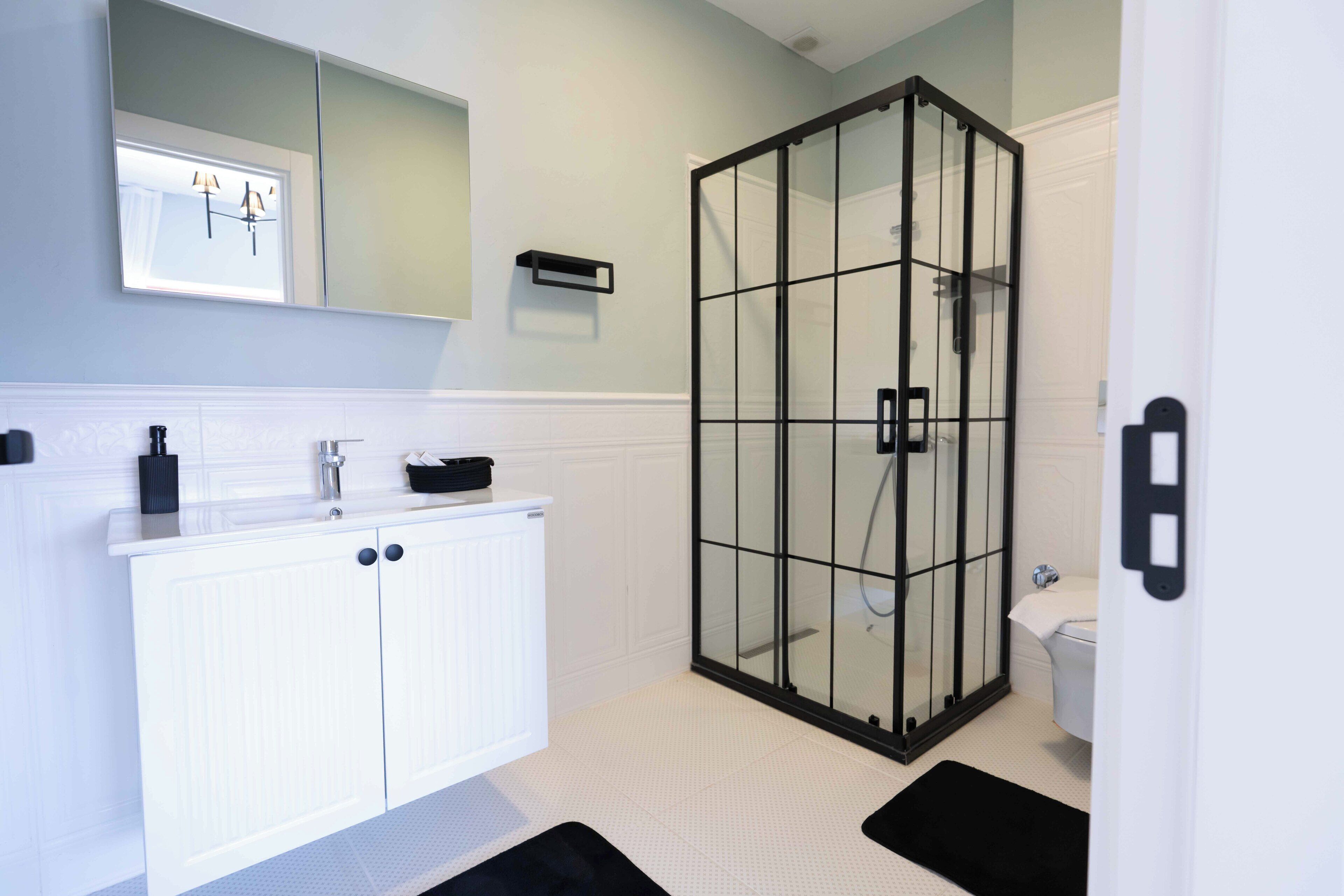 Et badeværelse med et hvidt håndvaskarrangement, en glasbrusekabine og et toilet.