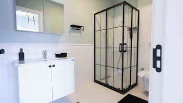 Une salle de bain avec un meuble-lavabo blanc, une cabine de douche en verre et des toilettes.