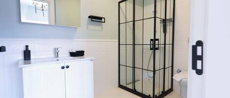 Et badeværelse med et hvidt håndvaskarrangement, en glasbrusekabine og et toilet.