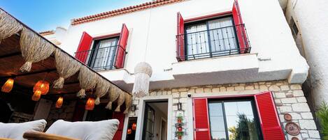 A building with red shutters, a stone facade, and a balcony with wicker furniture.