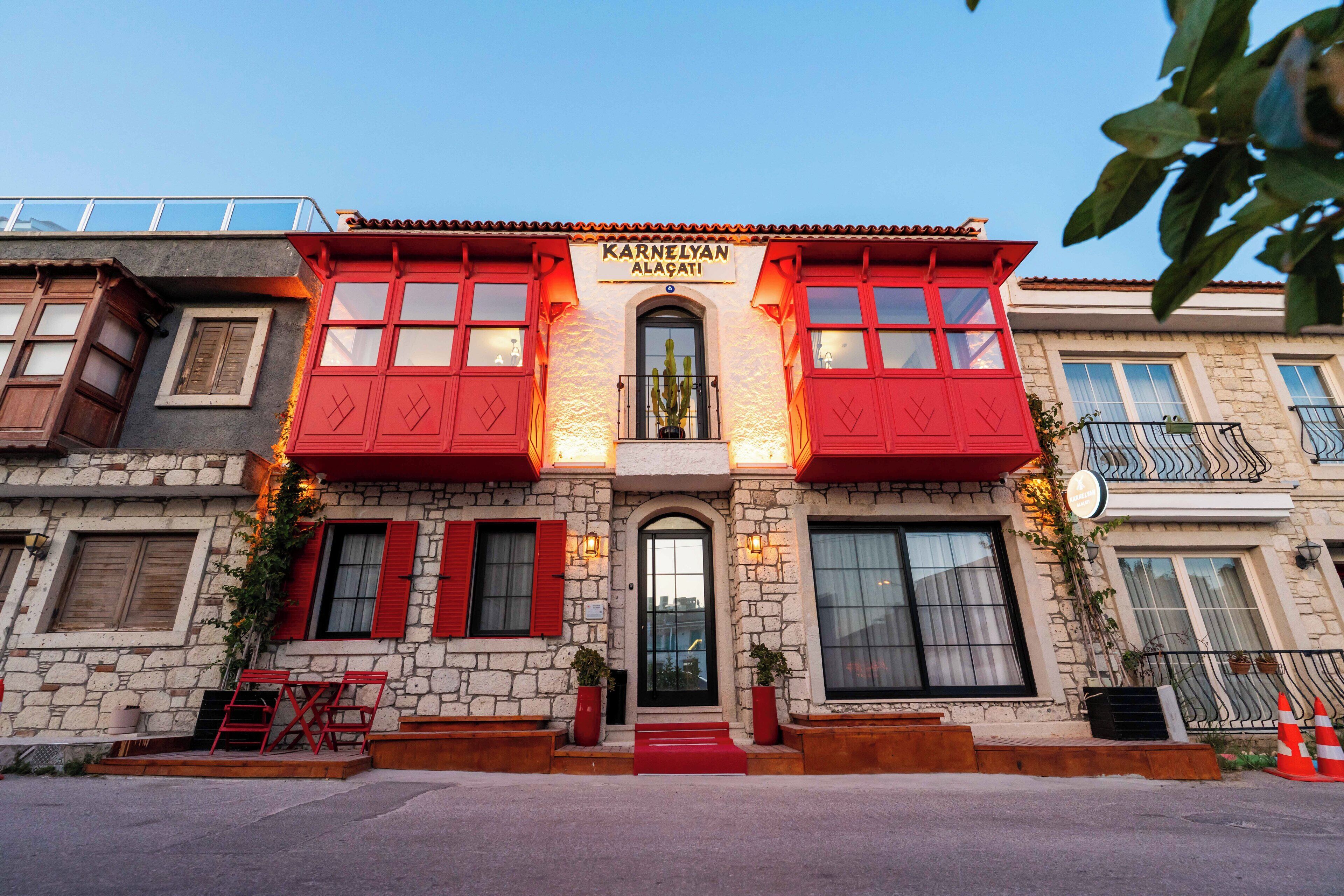 A two-story building with a stone facade, red shutters, and a sign reading "Karnelian Alagati".