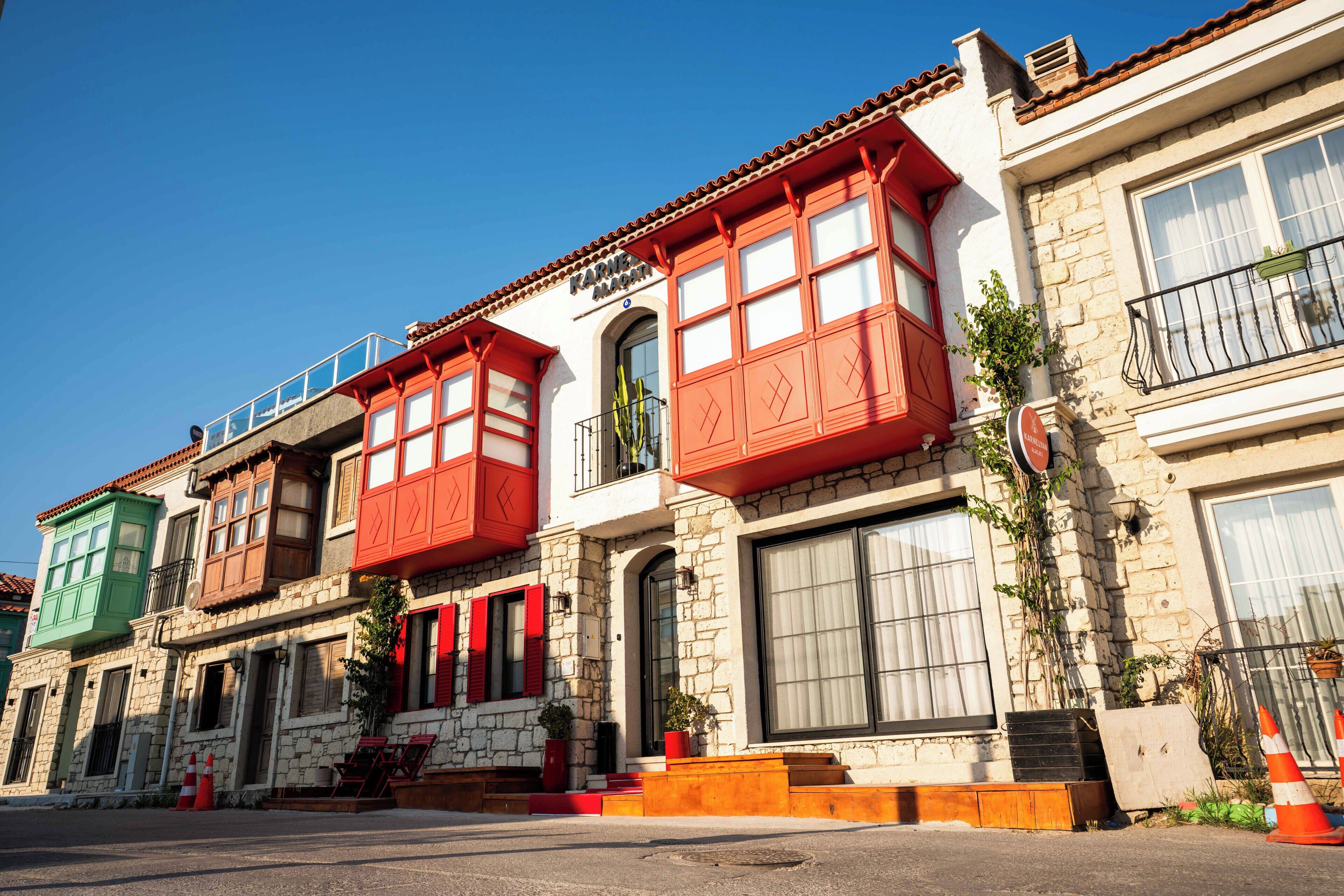 A row of traditional buildings with red and green facades, stone walls, and balconies.