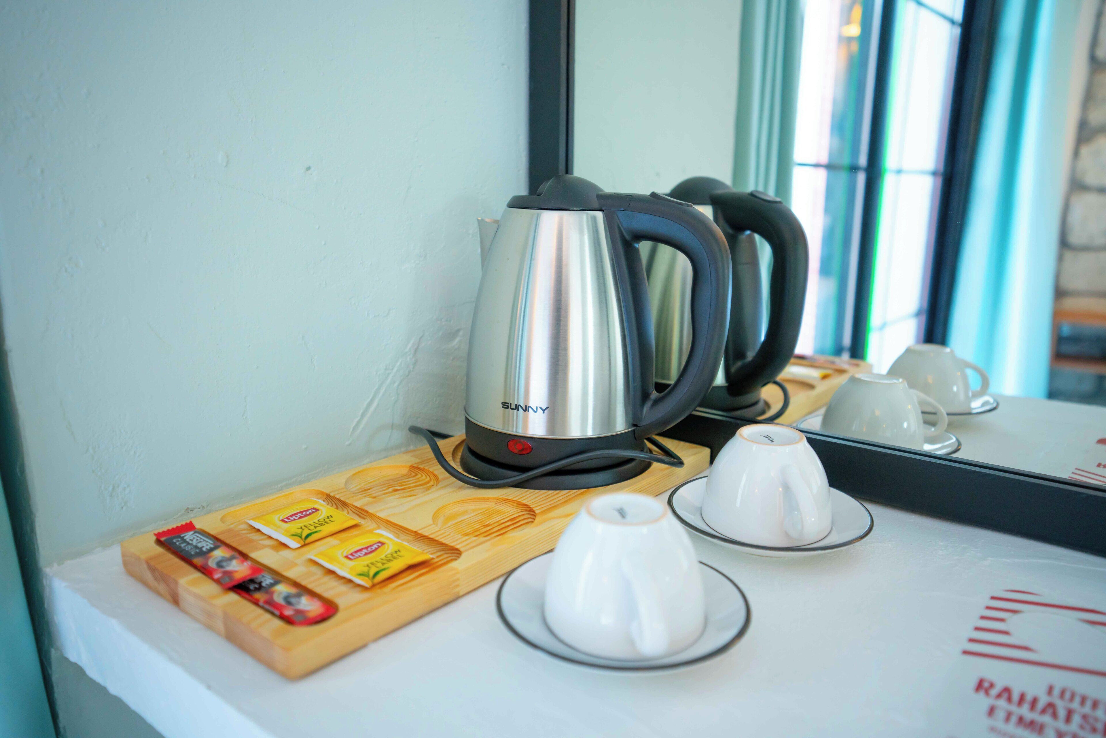 A kitchen counter with a kettle, tea cups, and a wooden cutting board with food items.