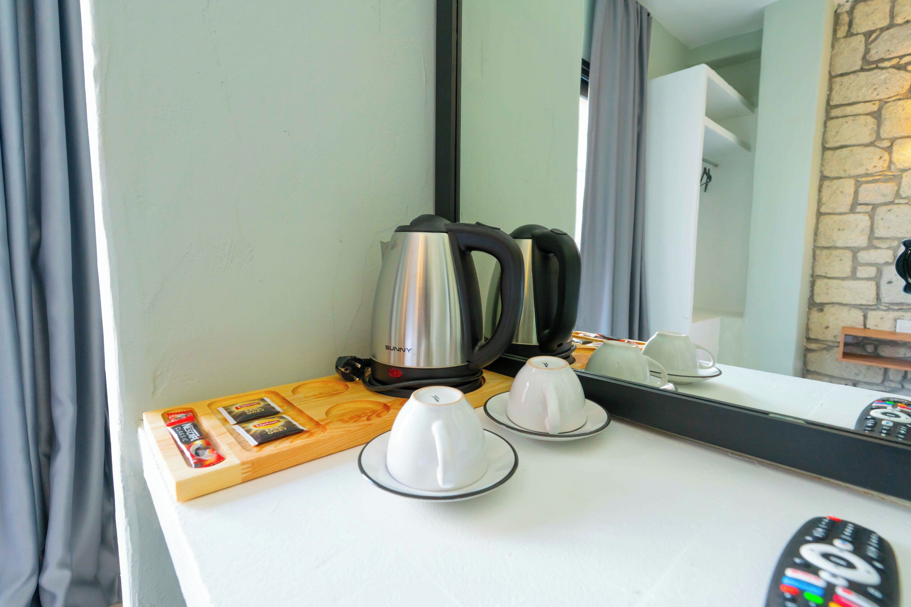 Ein Hotelzimmer mit einer weißen Arbeitsplatte, einer Kaffeemaschine, zwei weißen Tassen, einer Fernbedienung und einem Holztablett mit einer Zeitschrift.