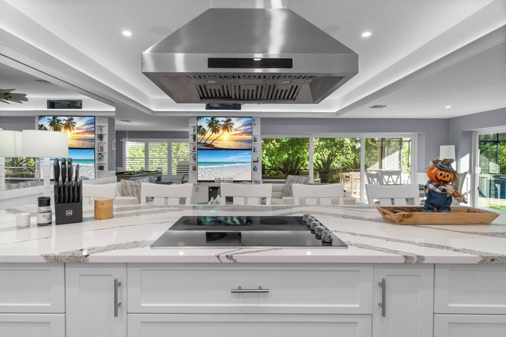 A modern kitchen with a large island, white cabinetry, and a stainless steel range hood.