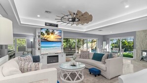 Een moderne woonkamer met een grote televisie, witte banken, een glazen salontafel en een plafondventilator.