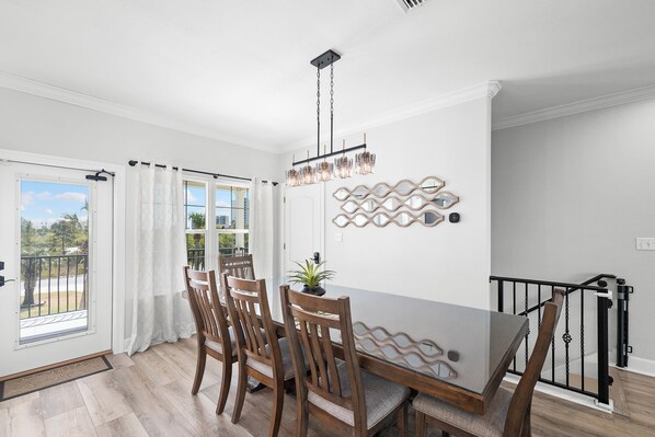 A dining area with a table, chairs, a hanging light fixture, a potted plant, and a decorative wall piece.
