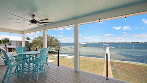 A covered outdoor area with a table and chairs, a ceiling fan, and a view of a body of water with a dock. - Spacious Perdido Key Retreat: Sand Volleyball, Dock, Gameroom & Beach (Pensacola)