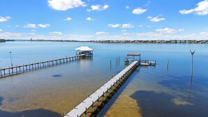 A pier extending into calm water with a covered seating area and a small boat docked at the end. - Spacious Perdido Key Retreat: Sand Volleyball, Dock, Gameroom & Beach (Pensacola)