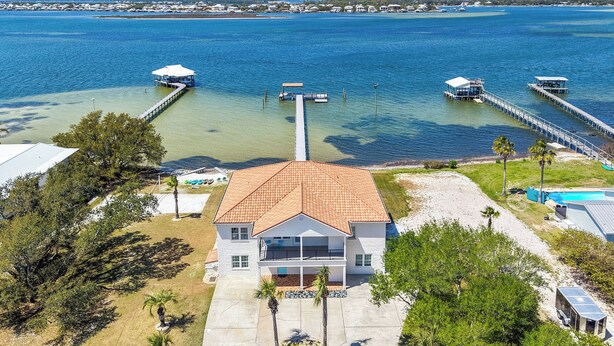 A house with a red roof, a dock extending into a body of water, and a clear view of the surrounding area. - Spacious Perdido Key Retreat: Sand Volleyball, Dock, Gameroom & Beach (Pensacola)