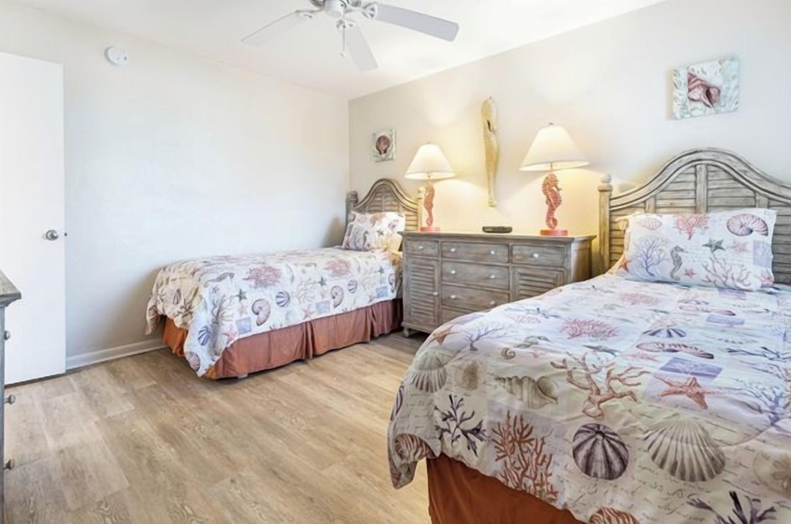 Une chambre avec deux lits, une commode et un ventilateur de plafond.
